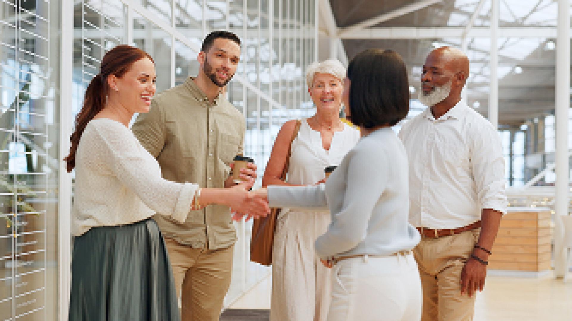 Five people in casual attire greet each other with smiles indoors.