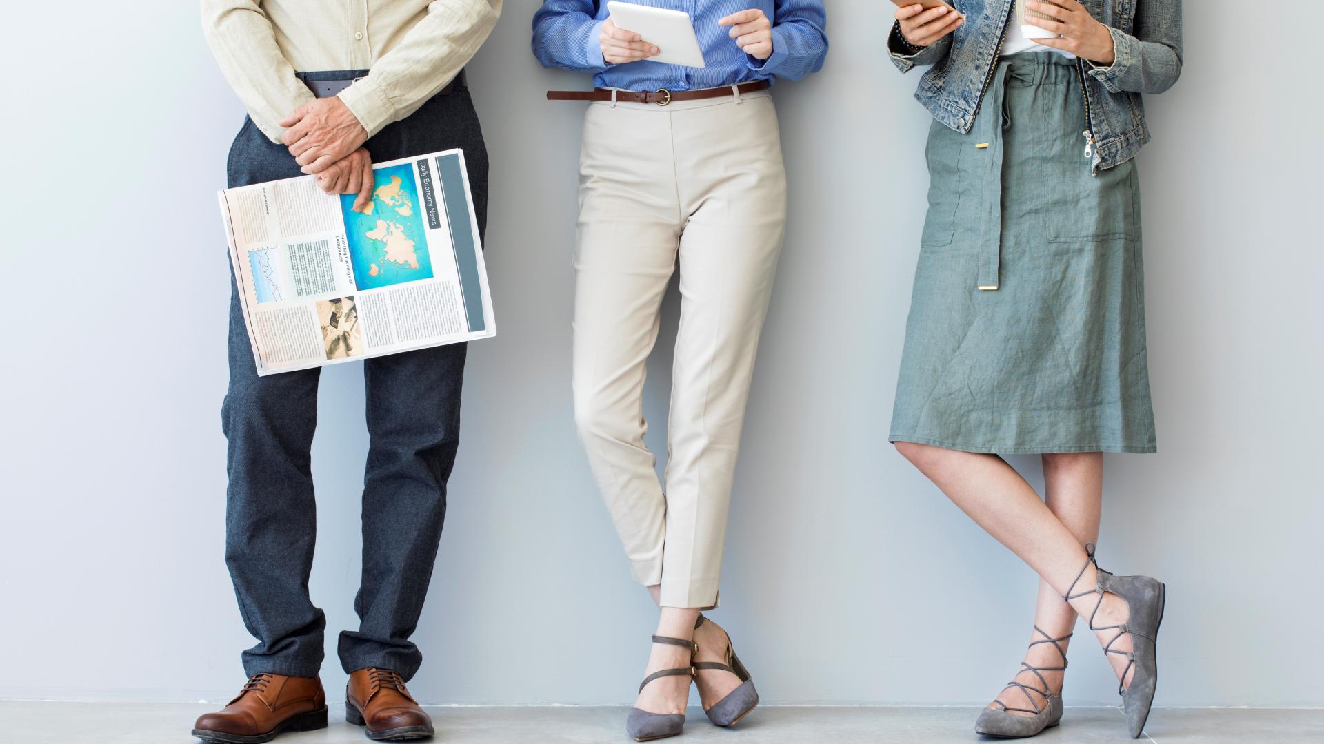 Trois personnes appuyées contre un mur tenant un journal, un téléphone portable et une tablette