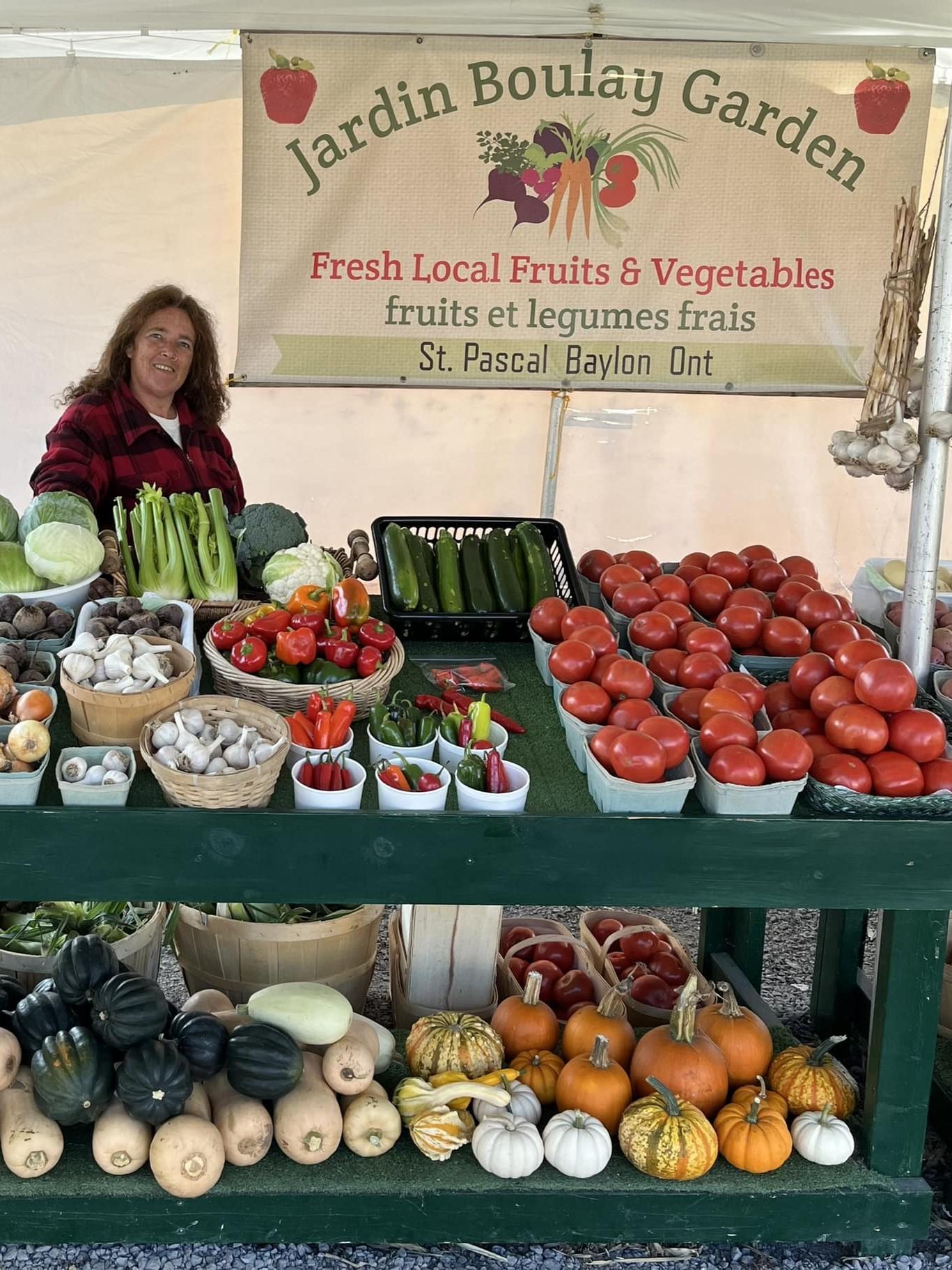 Owner of Jardin Boulay Garden is standing in the market stand behind a display of produce